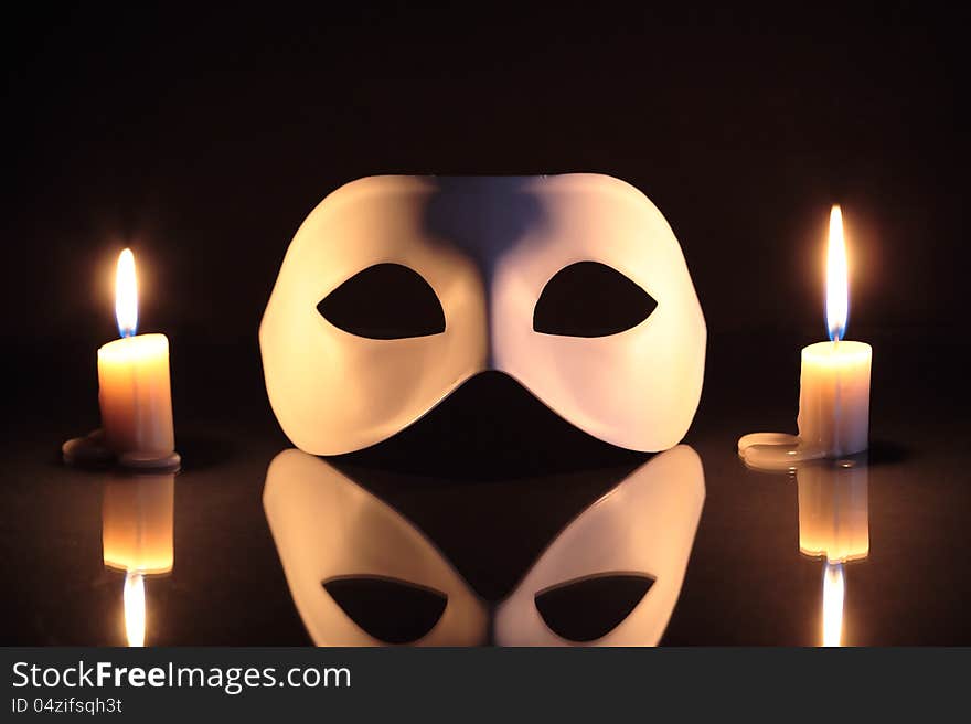 White mask between lighting candles on dark background. White mask between lighting candles on dark background