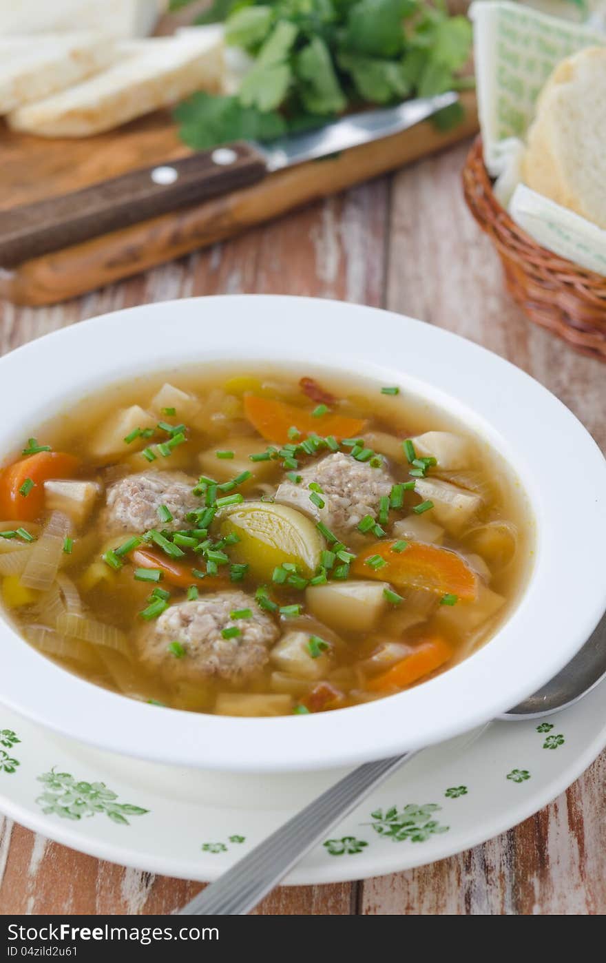 Plate of vegetable soup with meatballs on the wooden table vertical