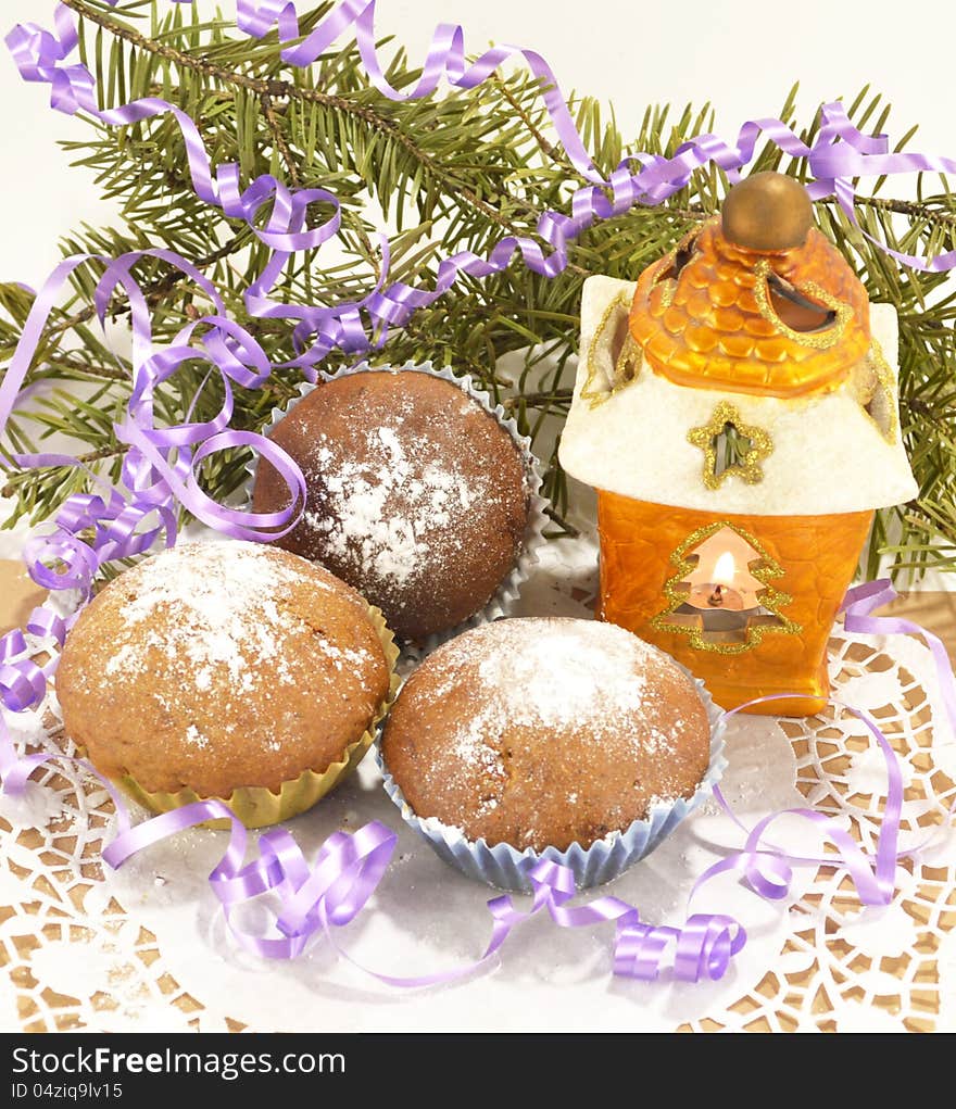 Three brown muffins with sugar powder, conifer and the yellow lantern. Three brown muffins with sugar powder, conifer and the yellow lantern