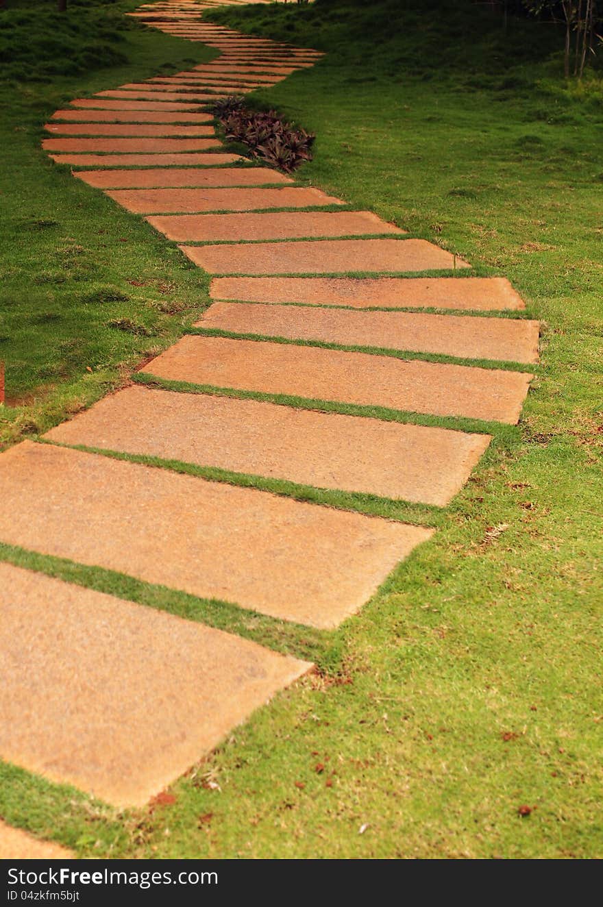 Walkway formed using granite stone slabs in a garden with lush green grass(lawn) on either side. The place is very tranquil and the walk way forms a S curve.