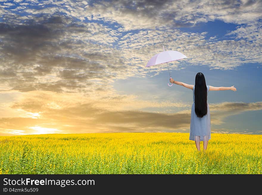 Asian girl holding pink umbrella in grass field and sunset