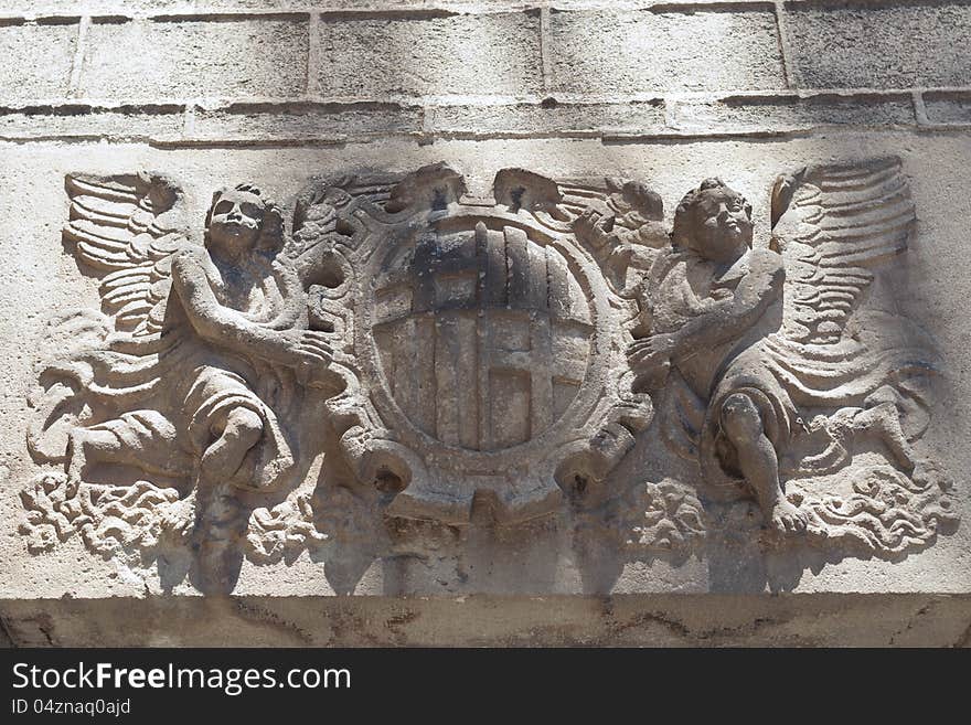 Medieval wall of Barcelona Cathedral with sculpture of two angels holding Coat of Arms. Medieval wall of Barcelona Cathedral with sculpture of two angels holding Coat of Arms