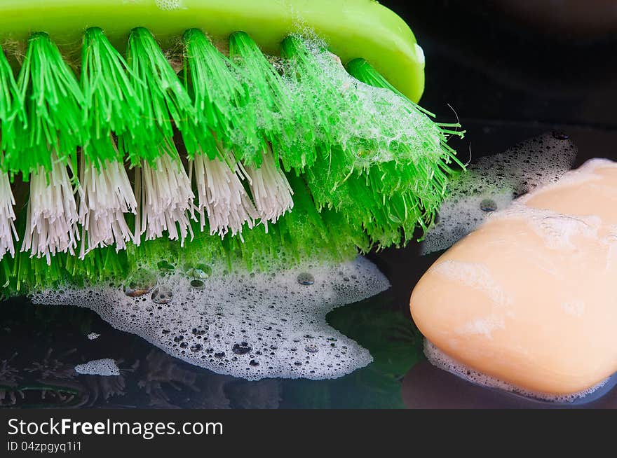 Brush for washing hands and a piece of green soap with foam shot against a black background. Brush for washing hands and a piece of green soap with foam shot against a black background