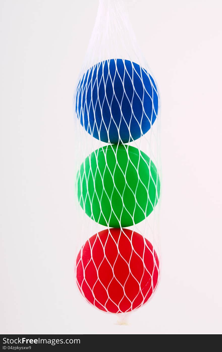 Three balls red, green and blue hanging in a white grid photographed close-up. Three balls red, green and blue hanging in a white grid photographed close-up