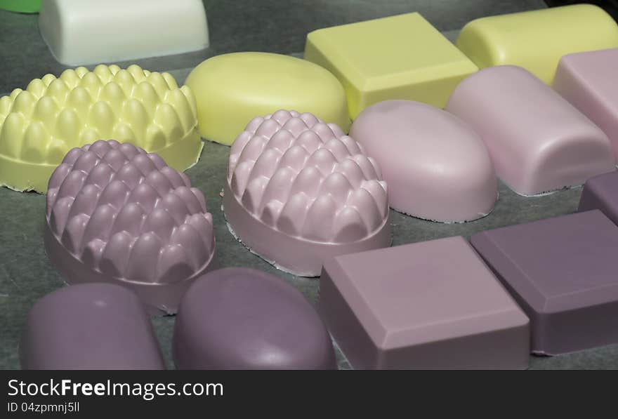 Rows of colorful homemade bath soaps drying on wax paper. Depth of field focused on molded images in the middle row.