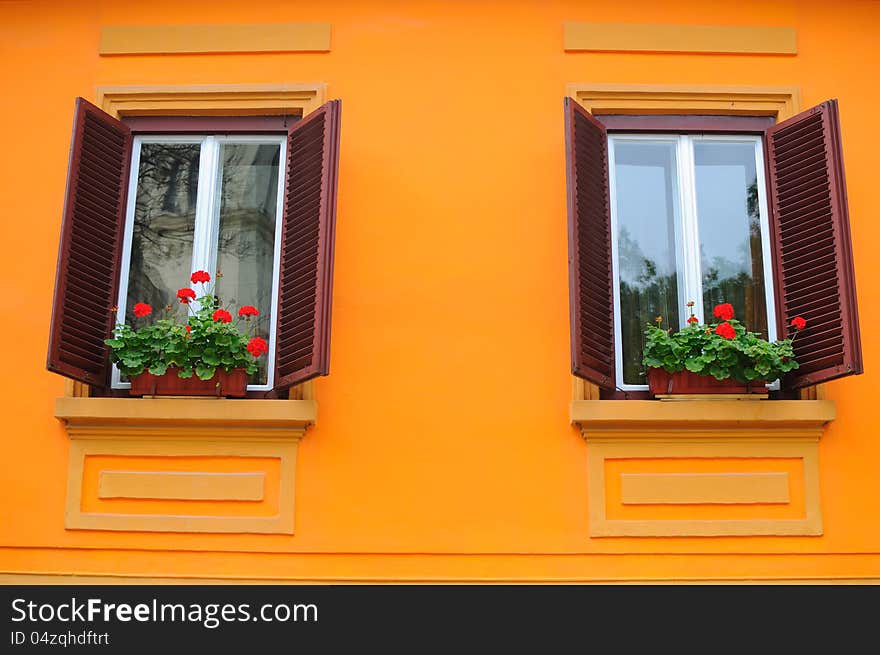 Orange wall with two traditional windows with wooden blinds and flowers on the sill. Orange wall with two traditional windows with wooden blinds and flowers on the sill.