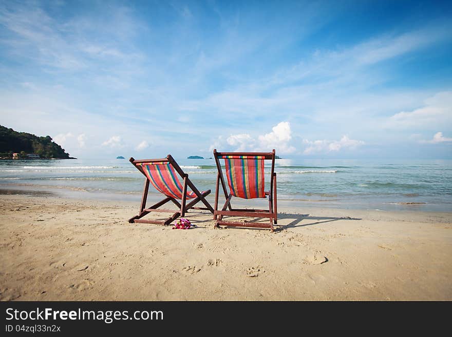 Two bright sun loungers on the beach. Bouquet of orchids in the sand.