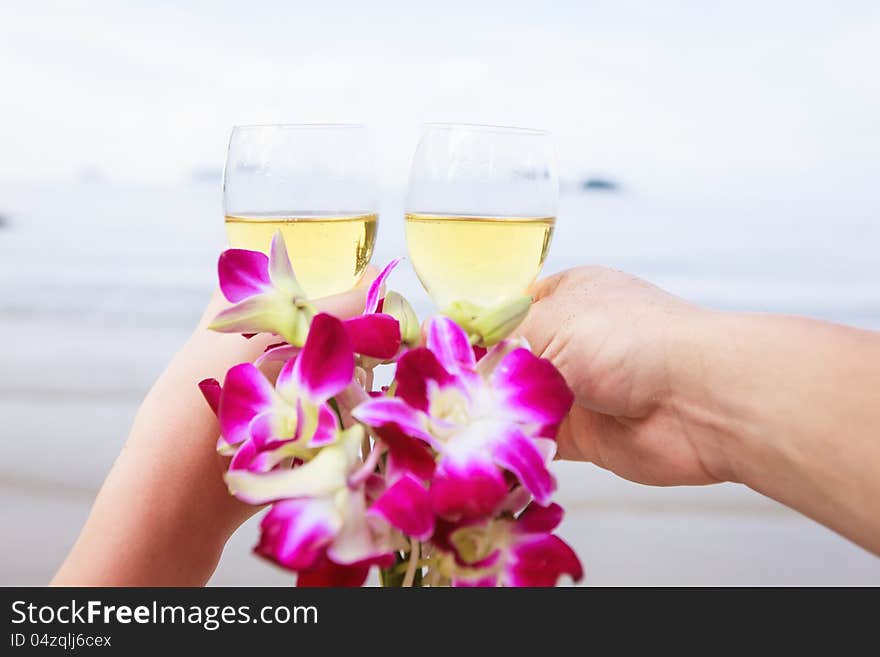 Two hands, glasses of champagne and a bouquet of orchids.