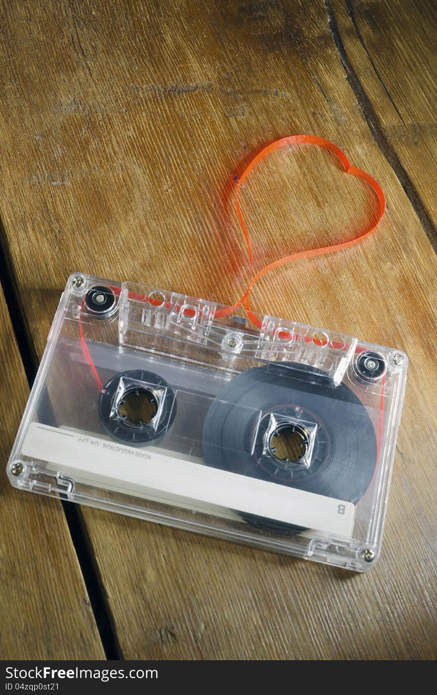 Vintage audio cassette on old wooden table with red tape pulled out as heart shape. Vintage audio cassette on old wooden table with red tape pulled out as heart shape