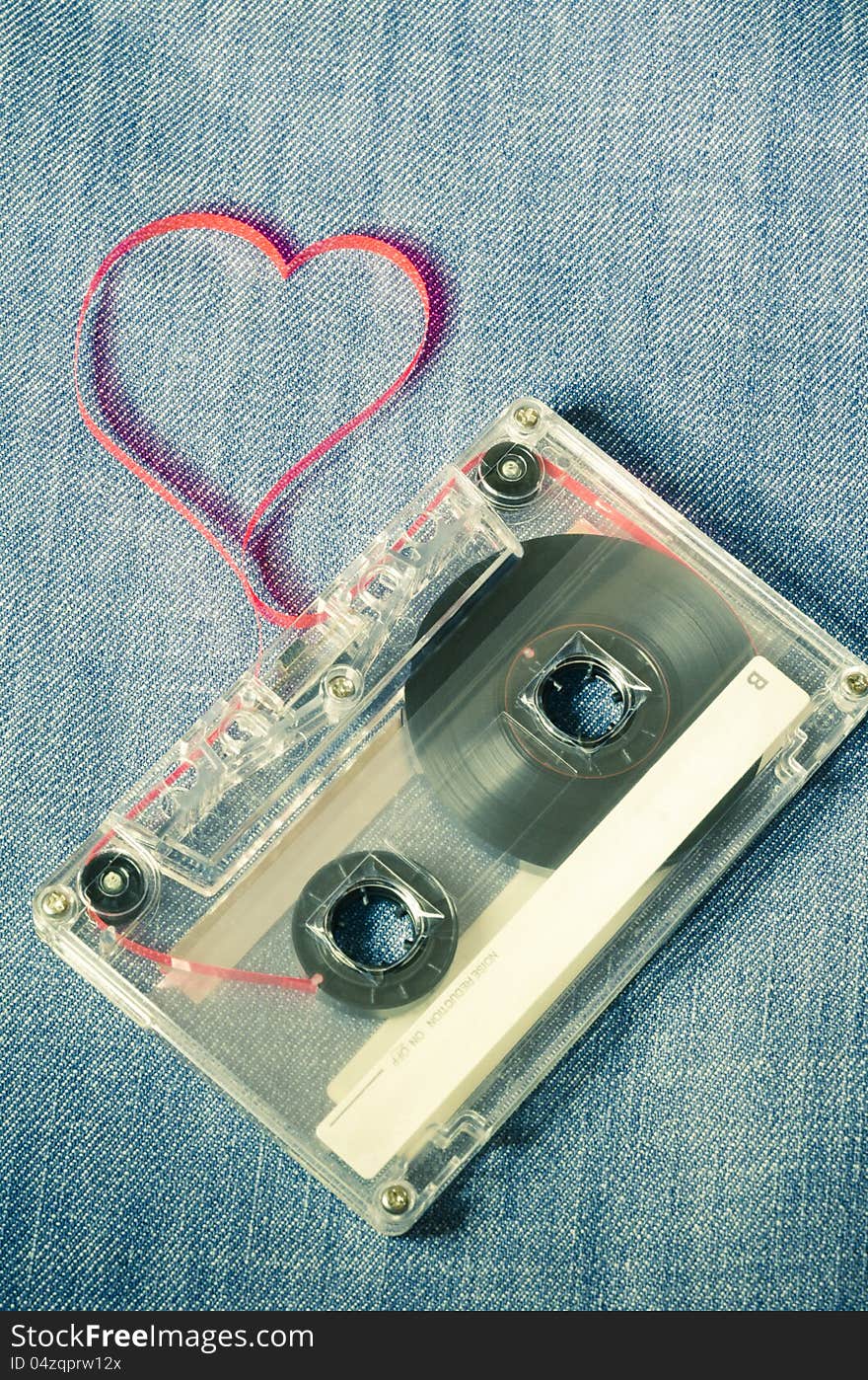 Vintage audio cassette on blue jeans with red tape pulled out as heart shape. Vintage audio cassette on blue jeans with red tape pulled out as heart shape