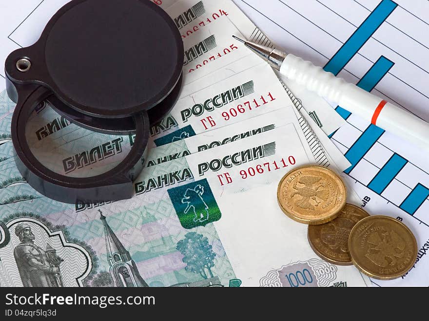 Metal and paper money, pencil and magnifying glass on a blue graph close-up