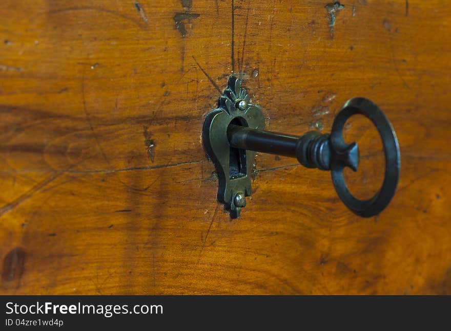 An old-style bronze key of a wooden furniture drawer, placed in its keyhole. An old-style bronze key of a wooden furniture drawer, placed in its keyhole