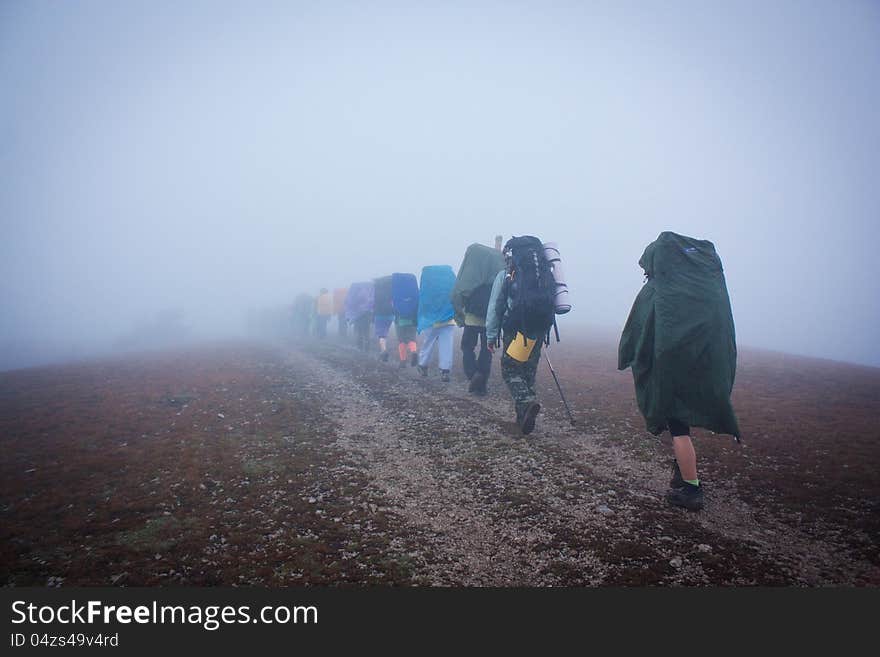 Group Of Tourists In Raincoats Disappearing Into Haze