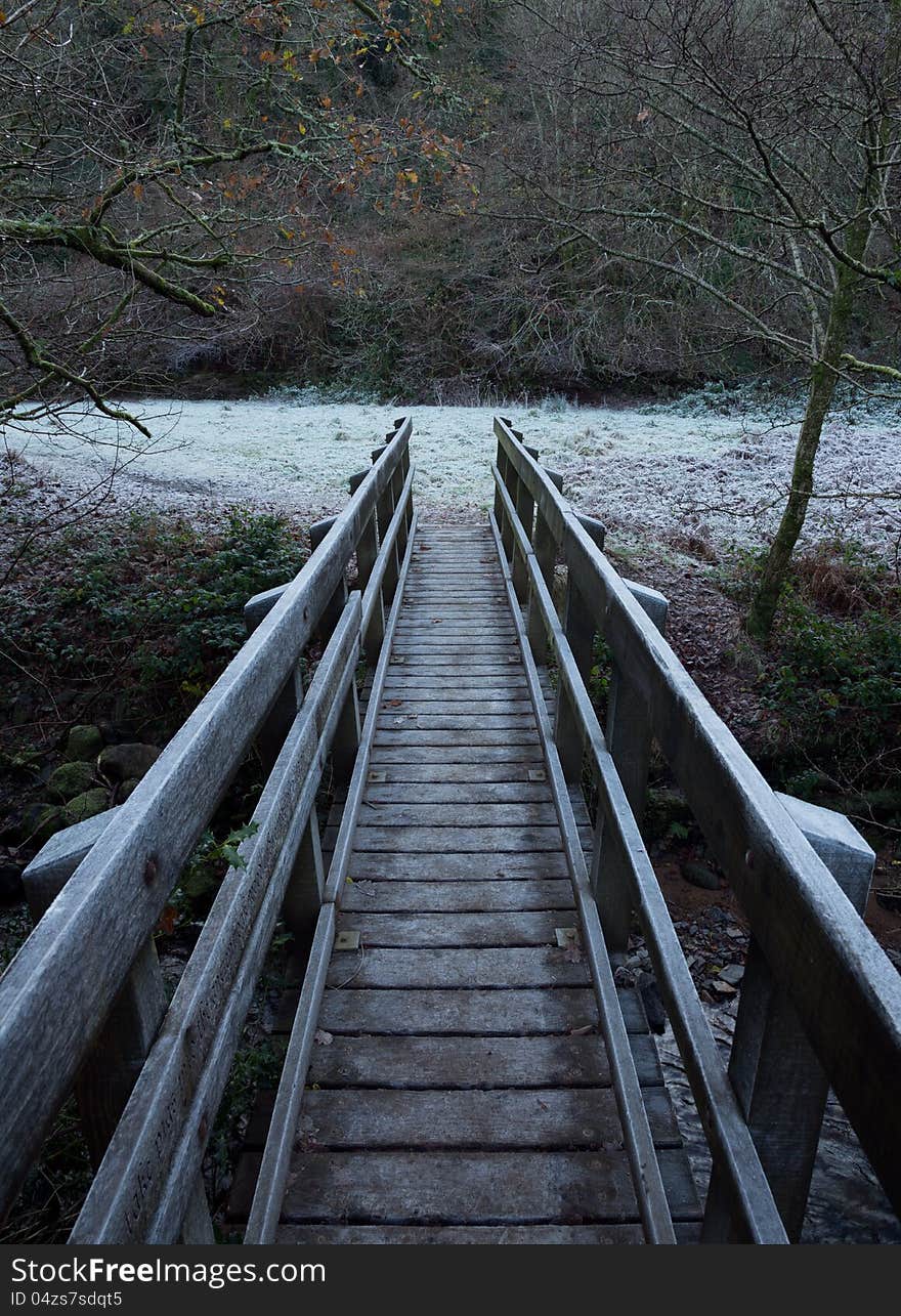 Wooden footbridge crossing a river with frost covering the rails and the grass in the field beyond. Wooden footbridge crossing a river with frost covering the rails and the grass in the field beyond.