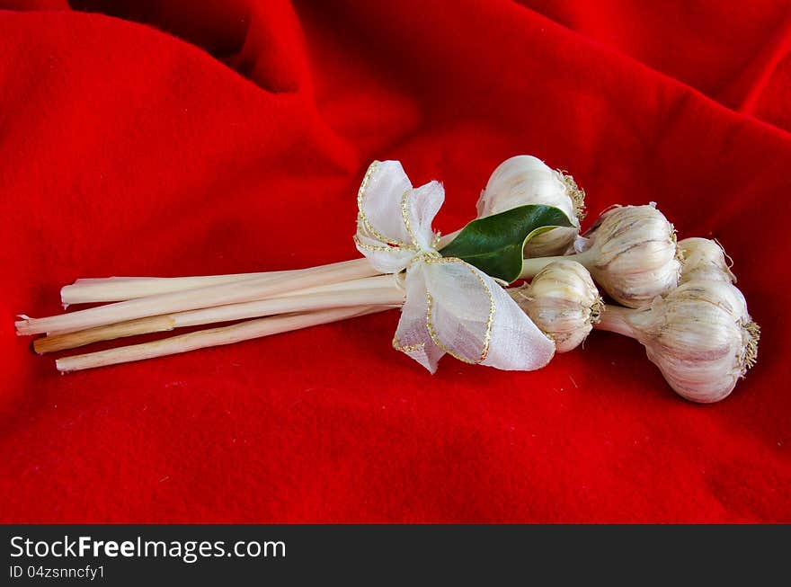 Bouquet of garlic bulbs tied with a white and gold ribbon for a Christmas gift on a background of red fabric.