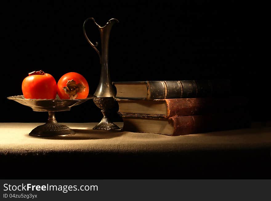 Vintage still life with persimmons in bowl near old book on canvas surface. Vintage still life with persimmons in bowl near old book on canvas surface