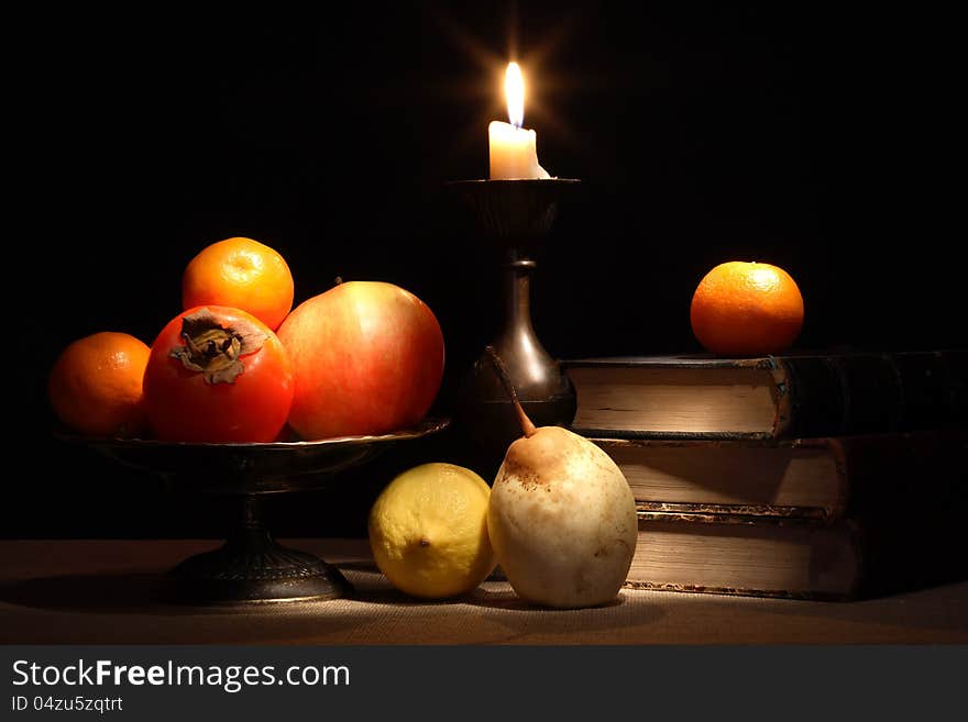 Vintage still life with fruits in bowl near old books and lighting candle. Vintage still life with fruits in bowl near old books and lighting candle