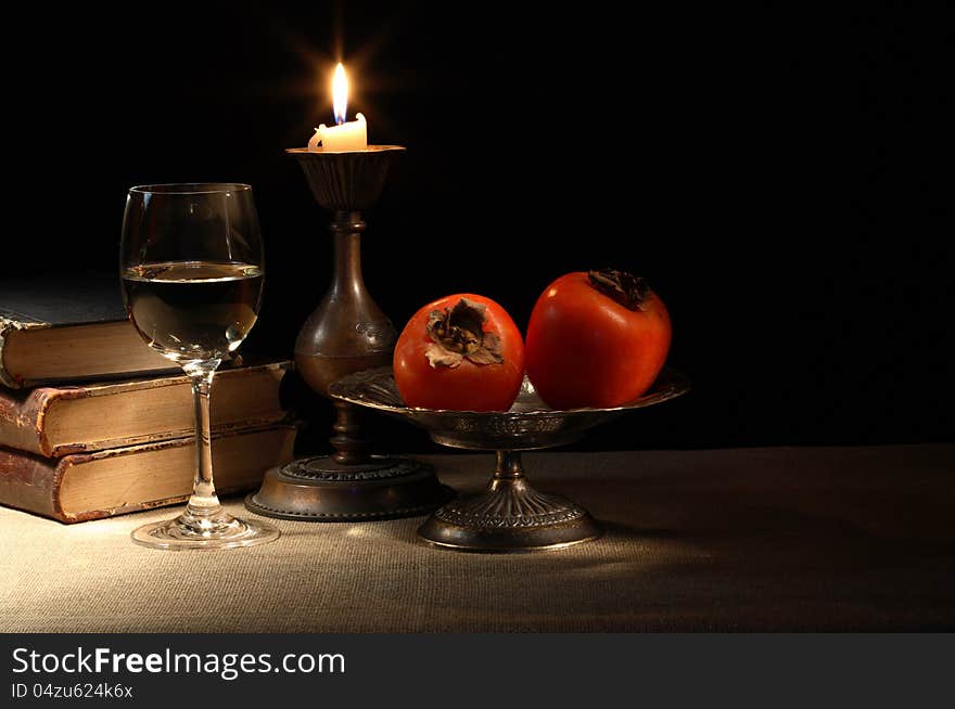 Vintage still life with fruits in bowl and wineglass near lighting candle and books