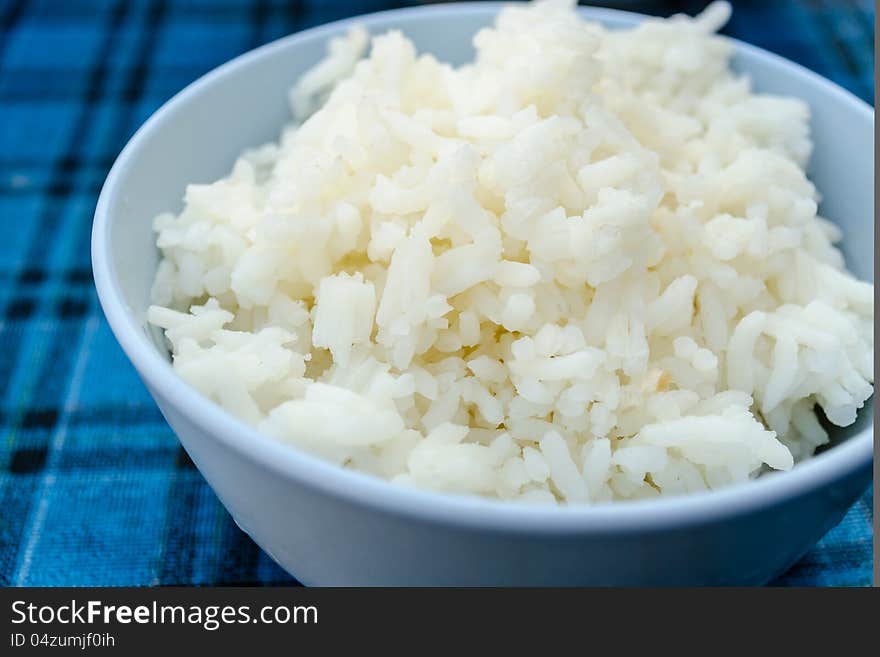 Thai jasmine rice in blue dish, on blue Plaid tablecloth.