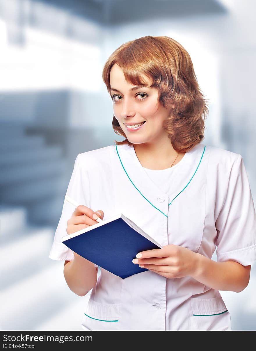 Young woman doctor in a white coat stands in hospital lobby. Young woman doctor in a white coat stands in hospital lobby