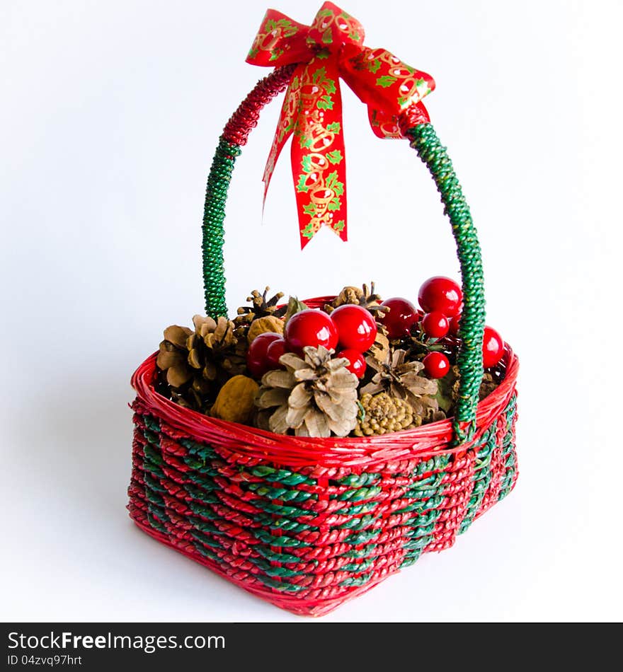 Decorative green and red wicker Christmas basket with a colorful ribbon on its handle and containing pine cones, nuts and cherries.