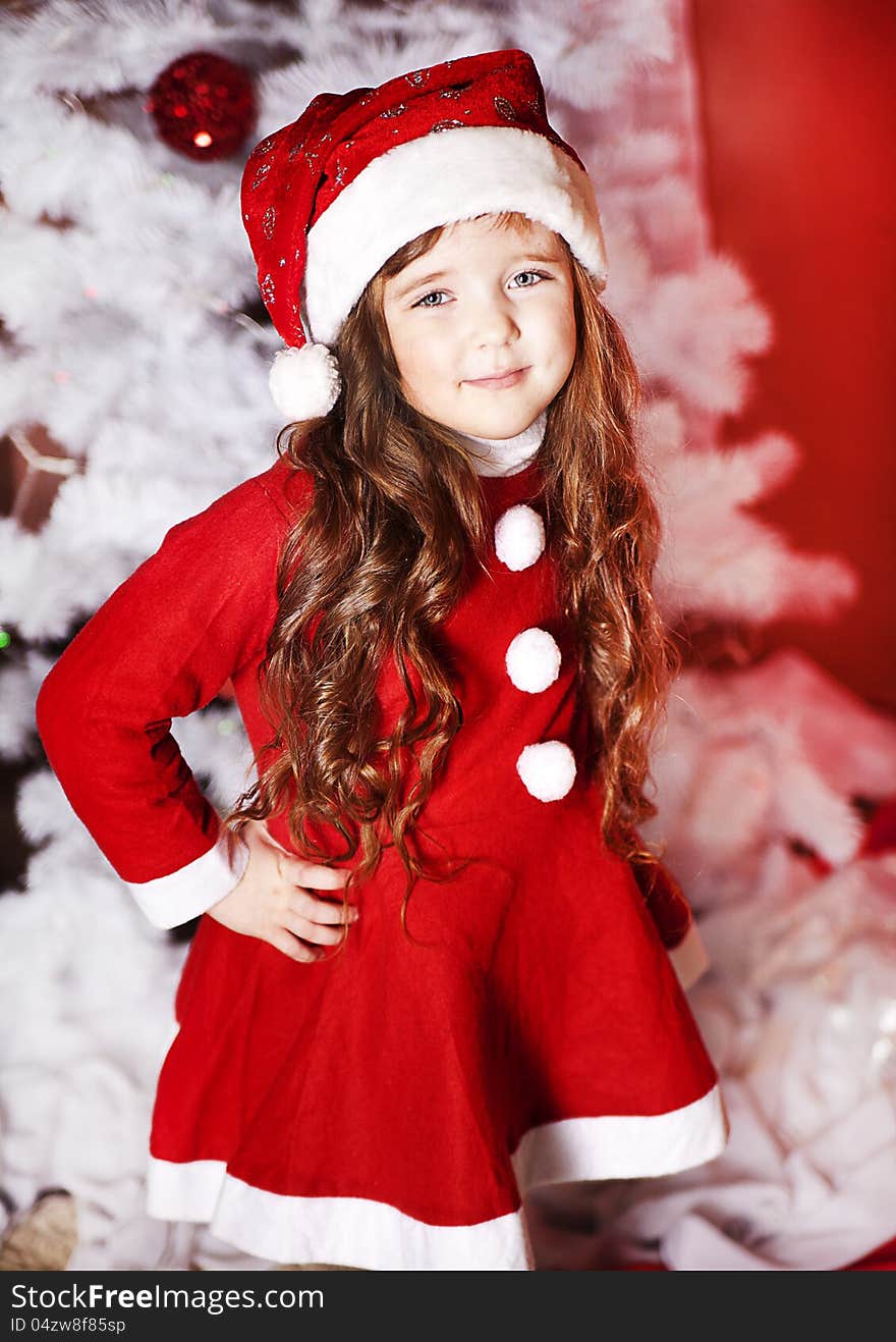 A little girl dressed as Santa Claus under the Christmas tree