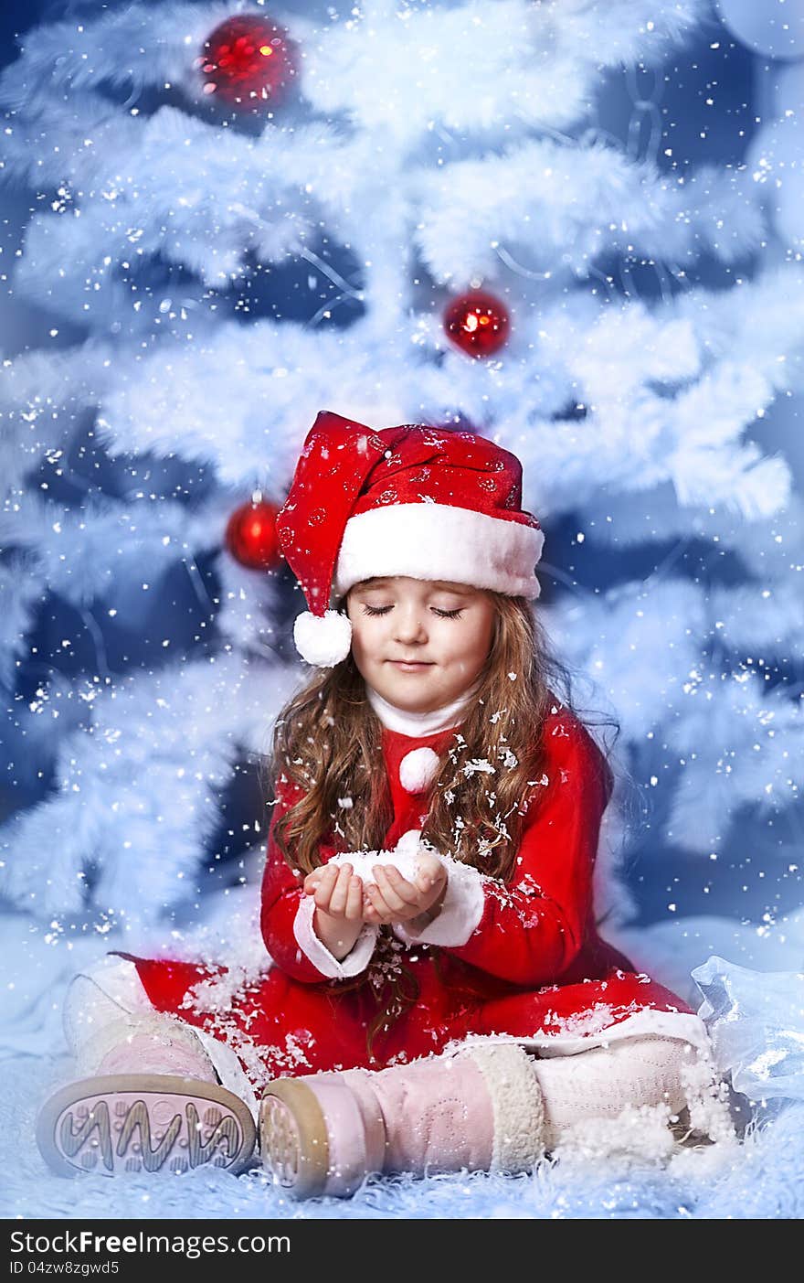 A little girl dressed as Santa Claus under the Christmas tree