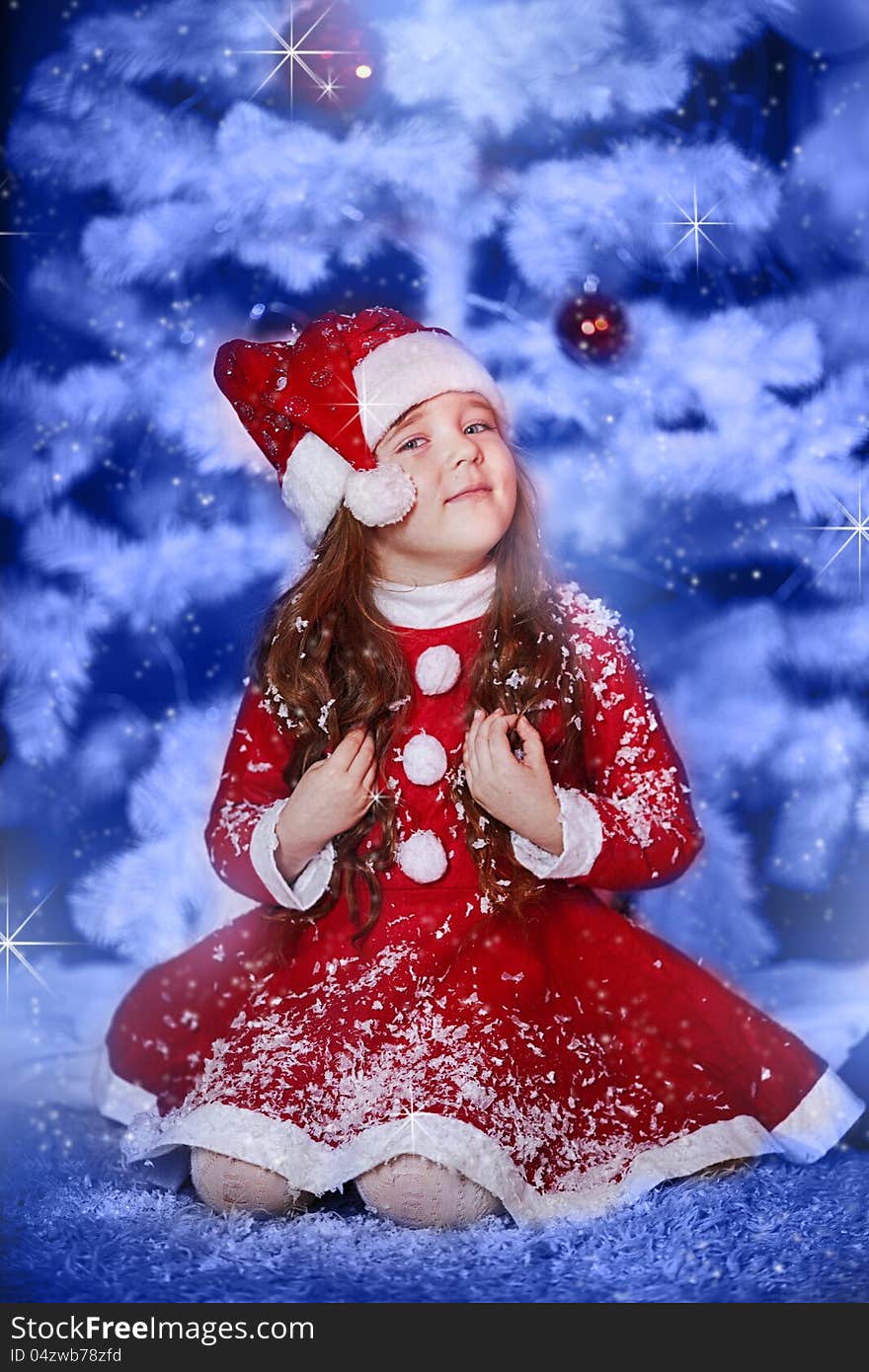 A little girl dressed as Santa Claus under the Christmas tree