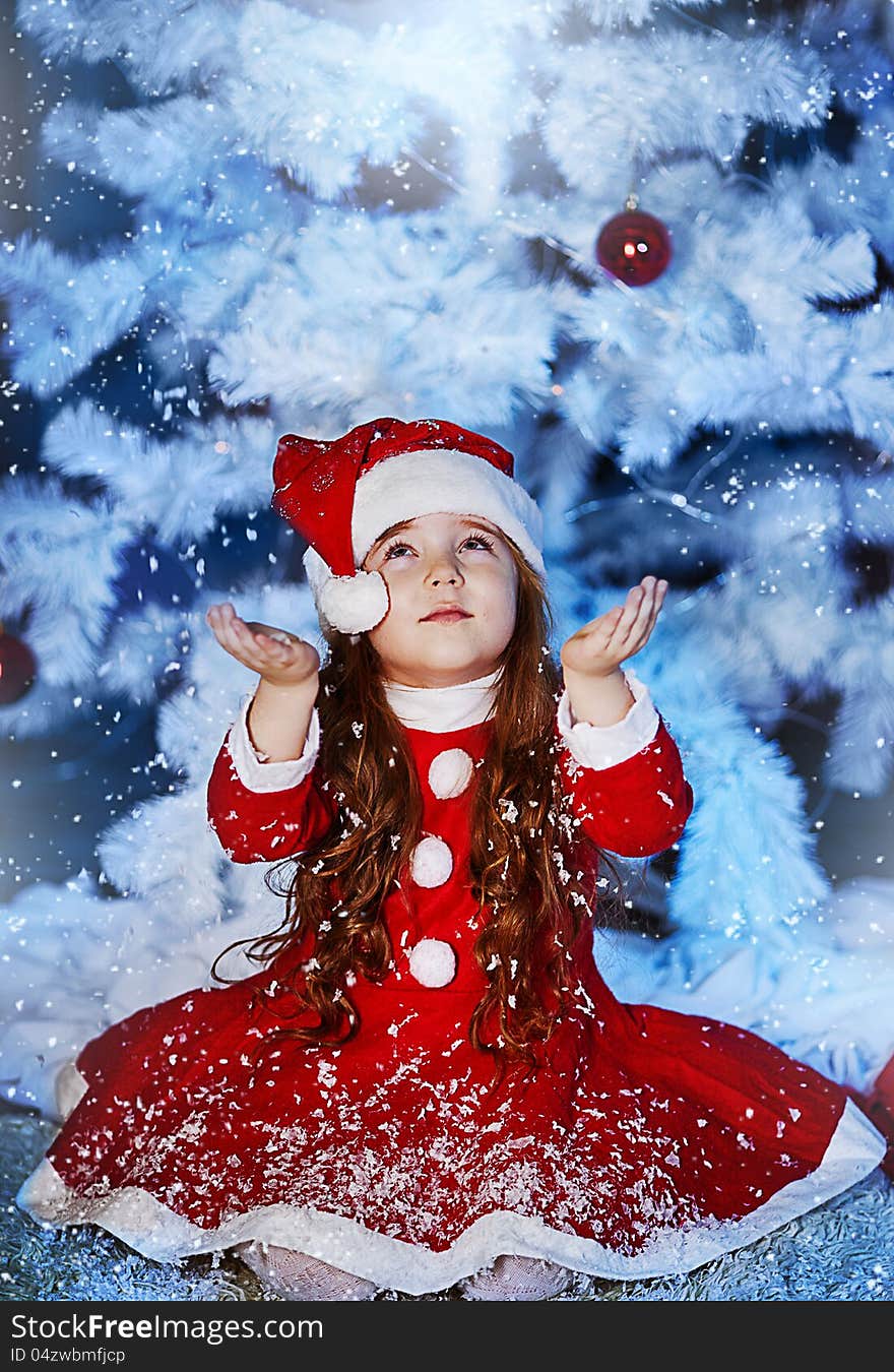 A little girl dressed as Santa Claus under the Christmas tree