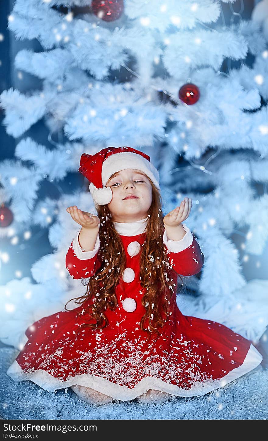 A little girl dressed as Santa Claus under the Christmas tree