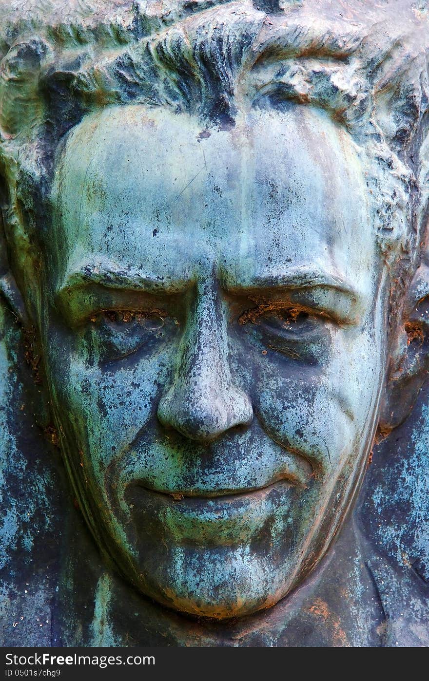 A closeup of a bronze verdigrised portrait of a man laughing