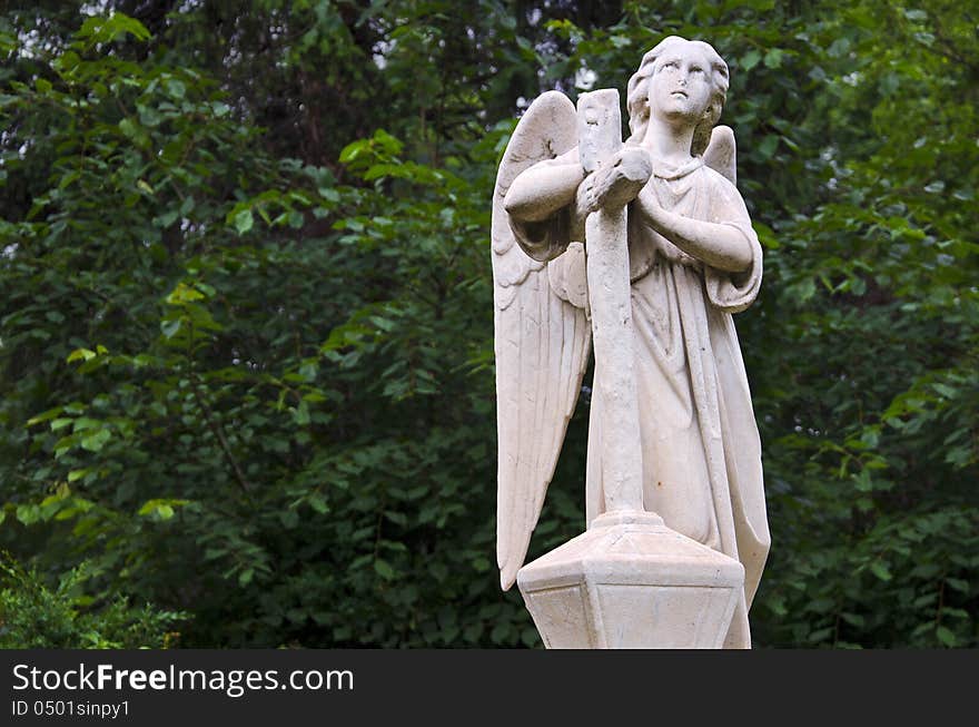 Angel statue looking towards sky on a green leafs background. Angel statue looking towards sky on a green leafs background