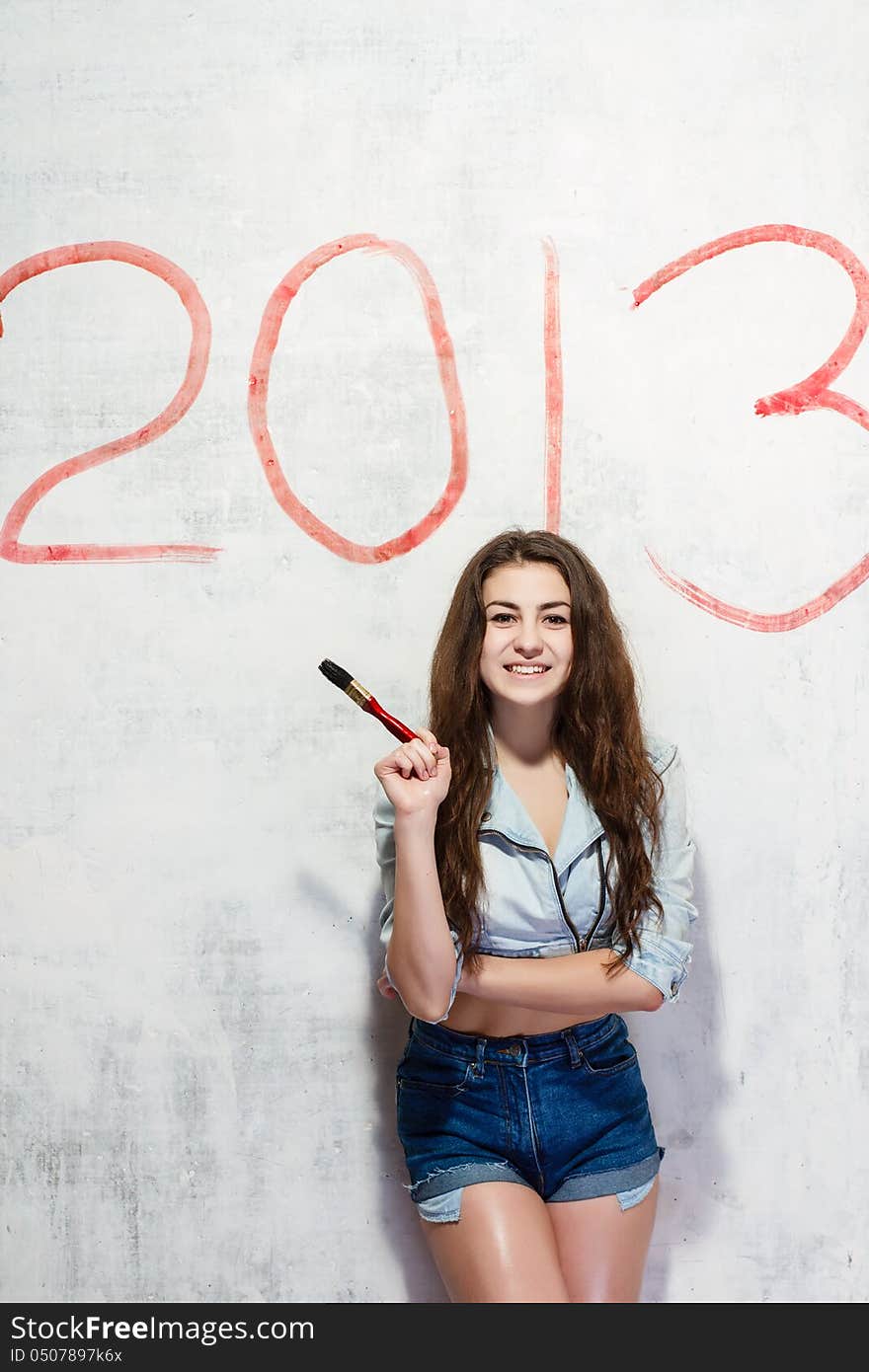 Girl in jeans shorts and jacket draws a Christmas (new year) decoration on old white wall with the red paint. Girl in jeans shorts and jacket draws a Christmas (new year) decoration on old white wall with the red paint.