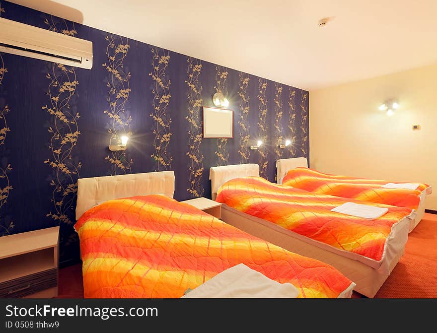 Interior of a hotel room for three persons, blue wallpapers and orange sheets on beds. Interior of a hotel room for three persons, blue wallpapers and orange sheets on beds.