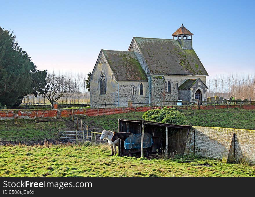 Photo of an ancient saxon church located in goodnestone,graveney in the rural county of kent with horses grazing in the field by their shelter. Photo of an ancient saxon church located in goodnestone,graveney in the rural county of kent with horses grazing in the field by their shelter.