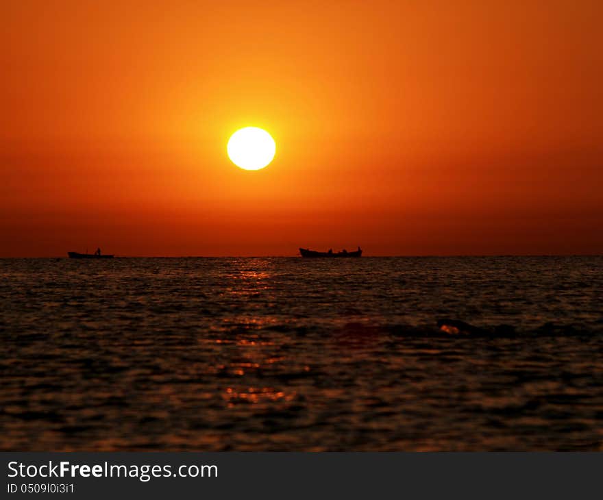 Fishing boat shapes on the horizon line and a man swimming towards them. Fishing boat shapes on the horizon line and a man swimming towards them