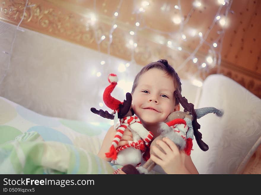 The boy woke up and sat on the bed with toy reindeer. The boy woke up and sat on the bed with toy reindeer