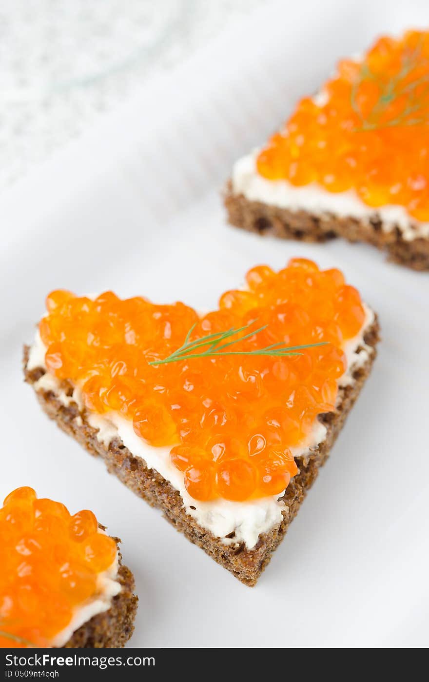 Sandwich with red caviar in the form of a heart on white plate