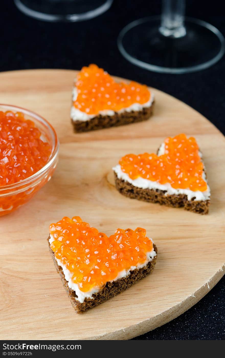 Three sandwich with red caviar in the form of a heart on a woode