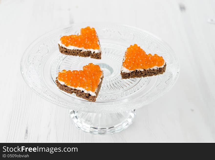 Three sandwich with red caviar in the form of a heart on glass stand base, horizontal