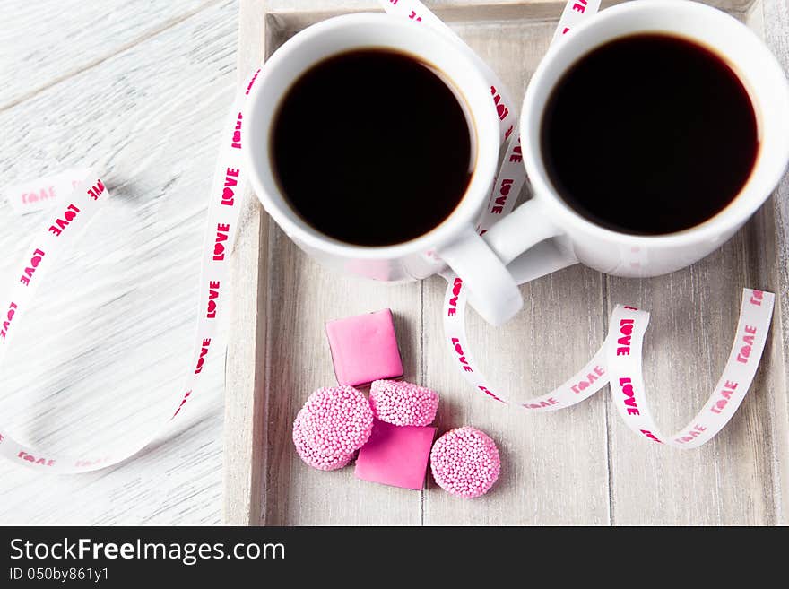 Two coffee cups with pink candies standing on the wooden tray