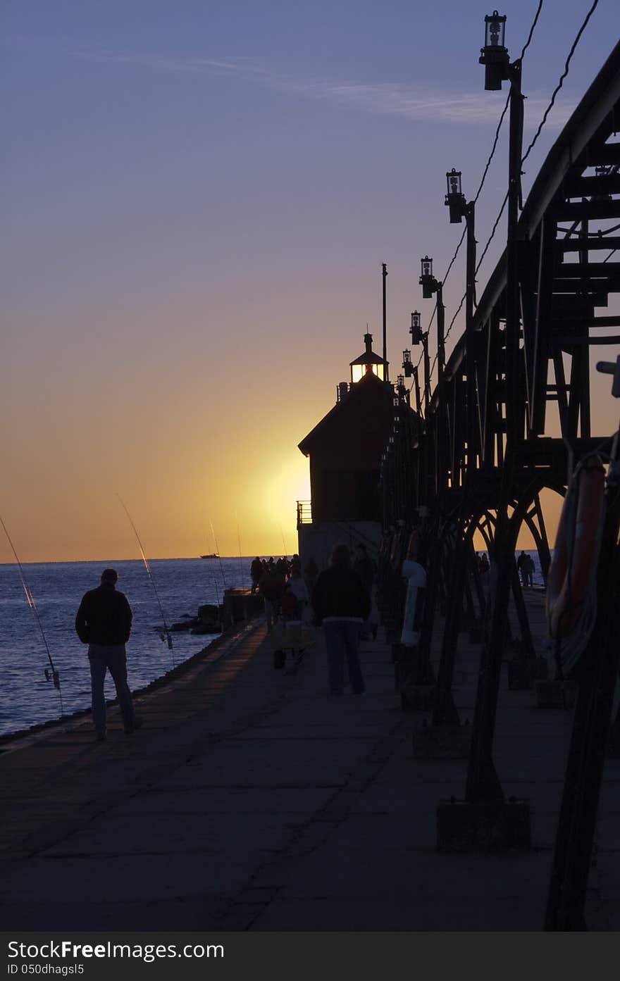 Lighthouse on lakeshore with elevated power supply at sunset with fisherman. Lighthouse on lakeshore with elevated power supply at sunset with fisherman