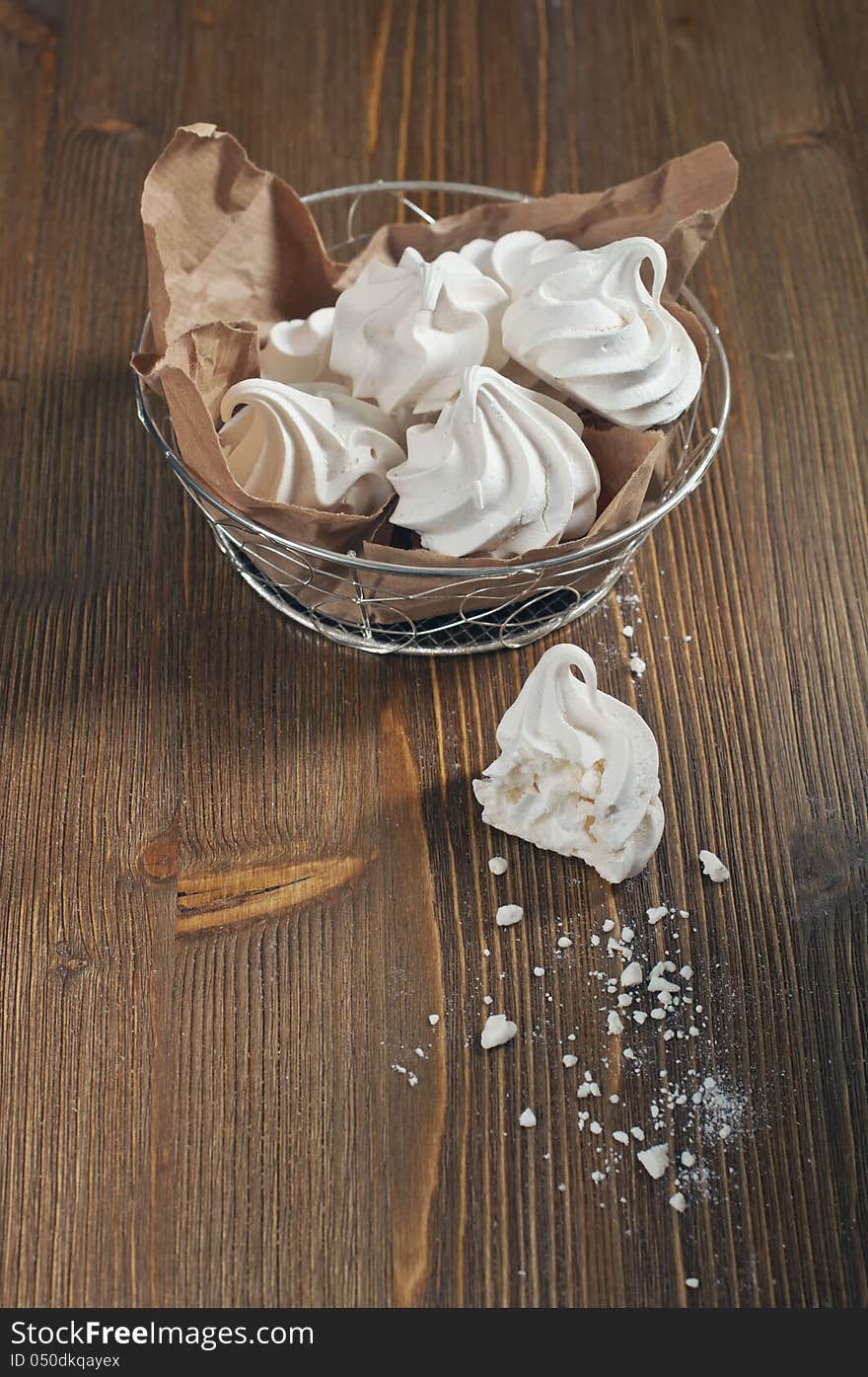 Top view of broken meringue with crumbs and lot of meringues in iron bowl on dark wooden background. Top view of broken meringue with crumbs and lot of meringues in iron bowl on dark wooden background