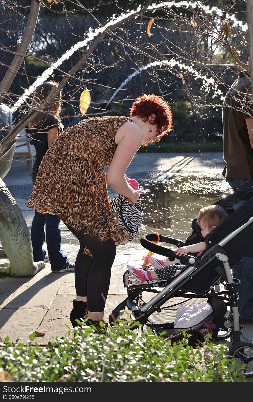 A mom with her one year old baby in a stroller in a park. Mom packing up baby stuff with stroller. A mom with her one year old baby in a stroller in a park. Mom packing up baby stuff with stroller.