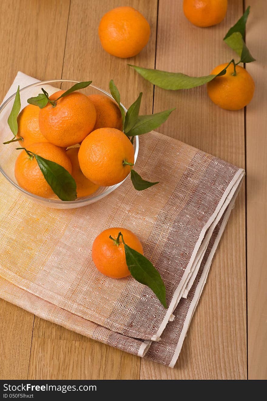 Mandarines with leaves in a glass bowl, on wooden table. top view. Mandarines with leaves in a glass bowl, on wooden table. top view