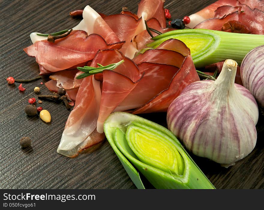 Arrangement of Jamon Slices, Ripe Leek, Garlic, Peppercorn and Rosemary closeup on Dark Wood background