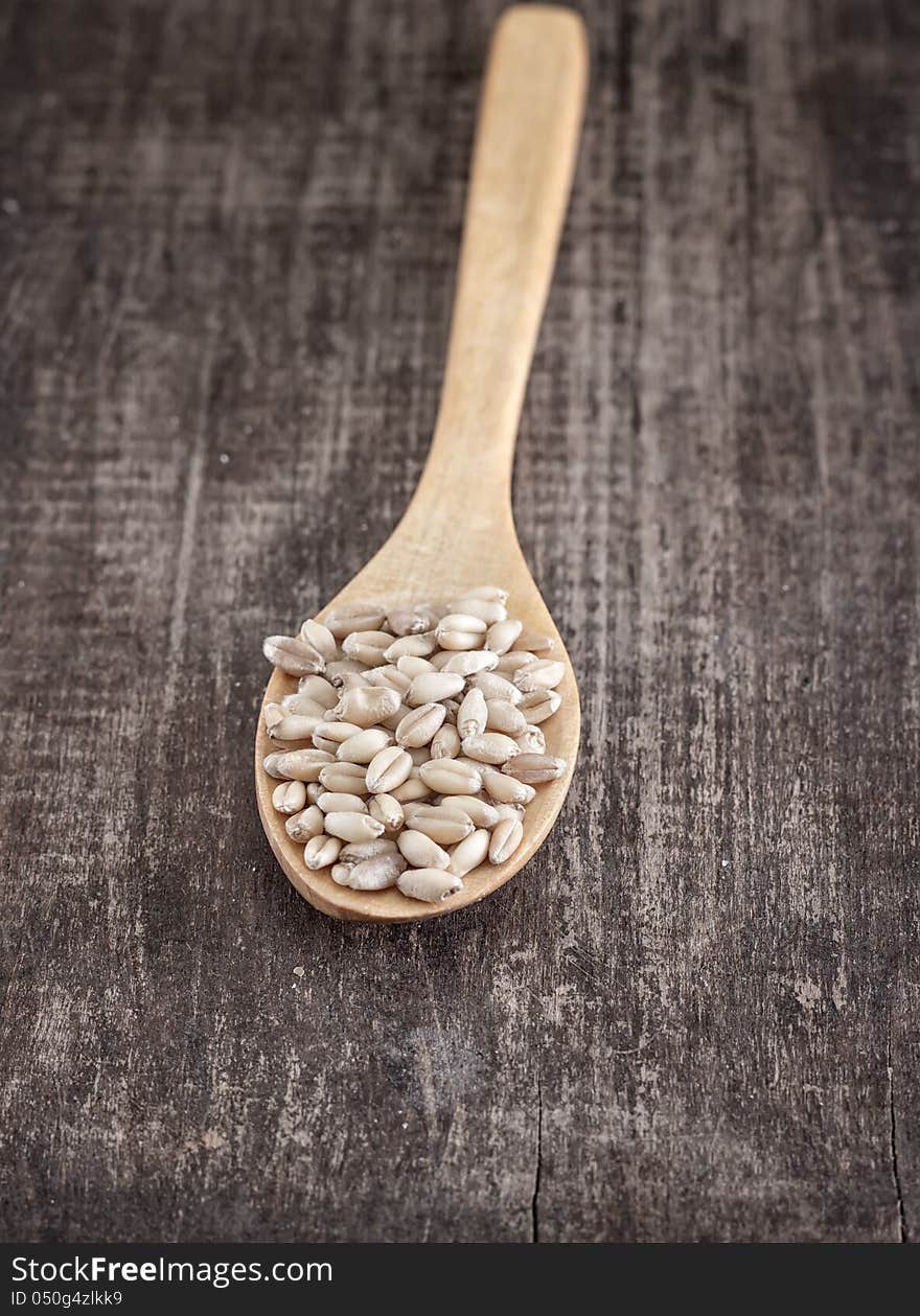 Wheat grain in the wooden spoon over old table