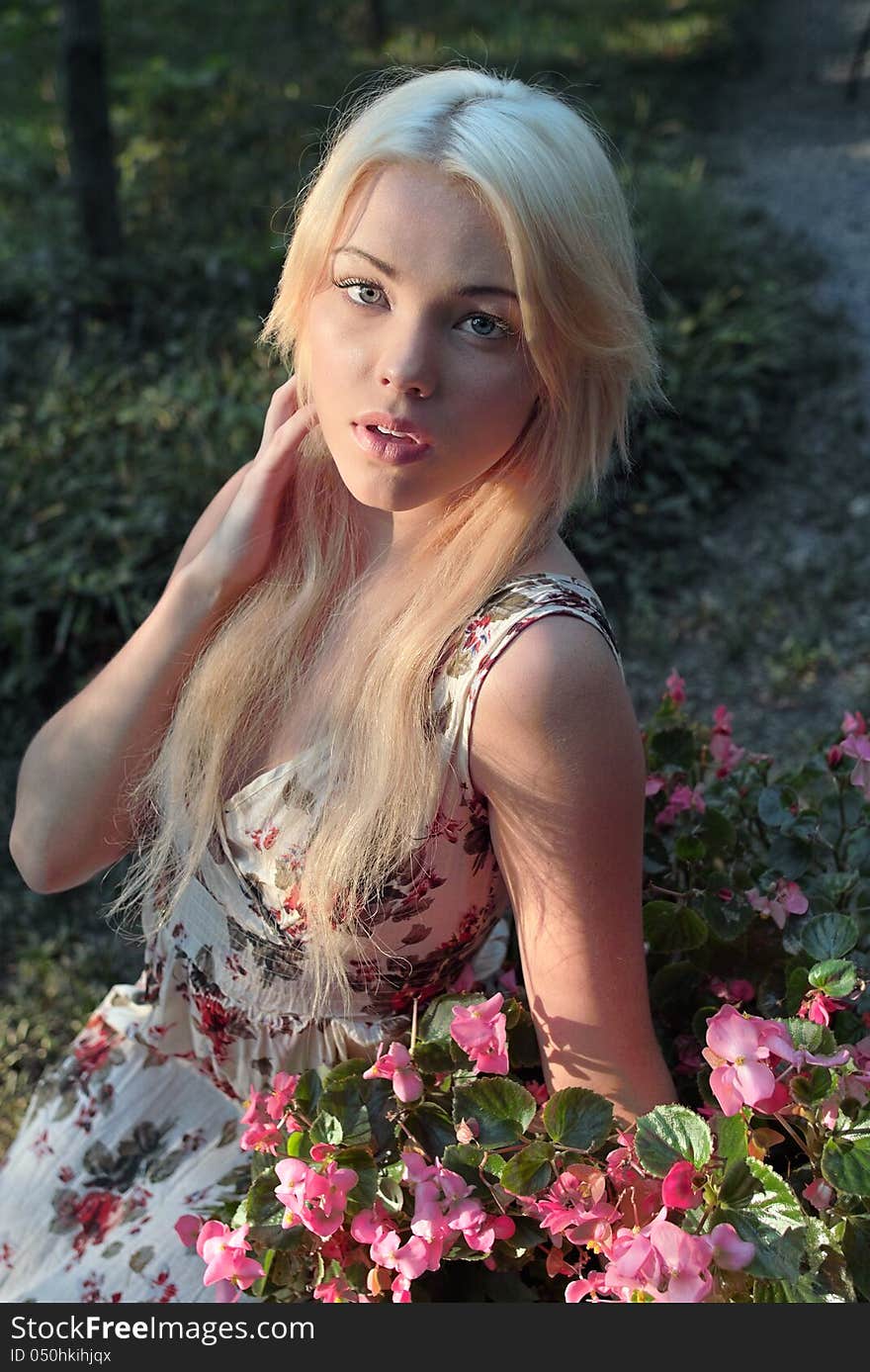 An image of a pretty woman sitting outside next to pink flowers. An image of a pretty woman sitting outside next to pink flowers