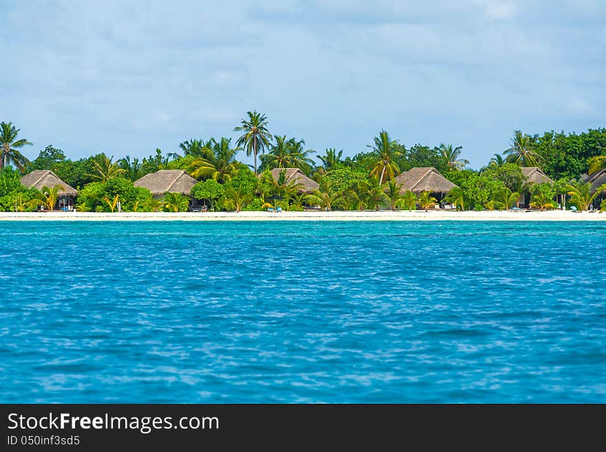 Tropical island hotel beautiful landscape with blue water, green trees, traditional bungalow and cloudy sky