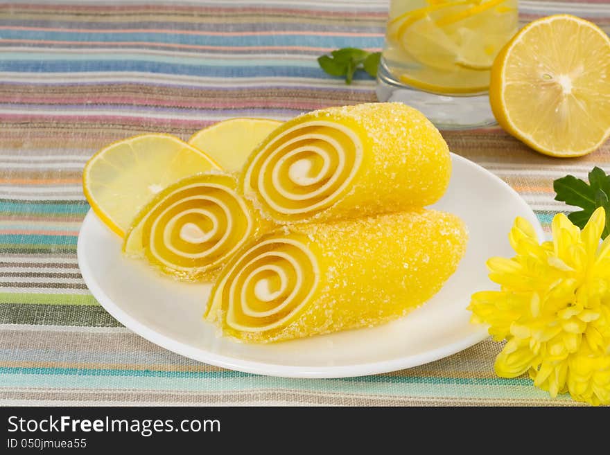 Yellow candy fruit on a plate with lemon and flower, closeup